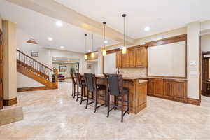 Kitchen with a kitchen breakfast bar, decorative light fixtures, light stone counters, kitchen peninsula, and backsplash