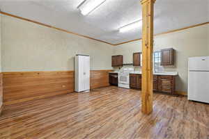 Kitchen featuring wood walls, white appliances, a textured ceiling, hardwood / wood-style flooring, and crown molding