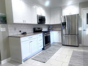 Kitchen featuring white cabinets, appliances with stainless steel finishes, quartz countertops, and decorative backsplash