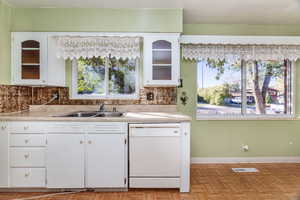 Kitchen with decorative backsplash, sink, light parquet style flooring, white cabinetry, and white dishwasher