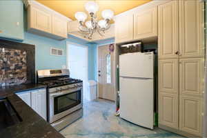 Kitchen with gas range, white fridge, dark stone counters, pendant lighting, and an inviting chandelier