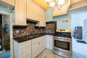 Kitchen featuring white cabinets, hanging light fixtures, sink, tasteful backsplash, and stainless steel range with gas cooktop