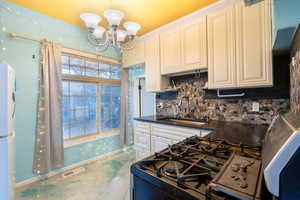 Kitchen with decorative backsplash, concrete floors, sink, white fridge, and a chandelier