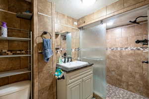 Bathroom with vanity, toilet, a textured ceiling, and tiled shower