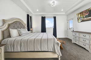 Bedroom with a tray ceiling, dark colored carpet, and multiple windows