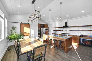 Dining space featuring a barn door, dark wood-type flooring, high vaulted ceiling, and sink