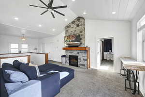 Living room featuring high vaulted ceiling, ceiling fan, a stone fireplace, and carpet flooring