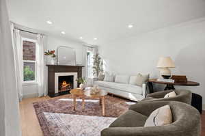 Living room with light hardwood / wood-style flooring, a tiled fireplace, and crown molding