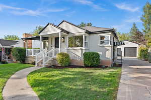 Bungalow-style house with a garage, a porch, a front yard, and an outbuilding