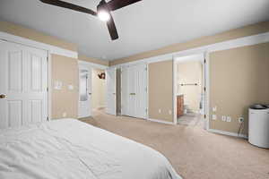 Bedroom featuring ceiling fan, multiple closets, ensuite bath, and light carpet