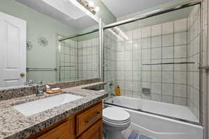 Full bathroom with enclosed tub / shower combo, vanity, and toilet