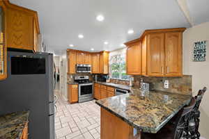 Kitchen with sink, kitchen peninsula, dark stone counters, a breakfast bar area, and appliances with stainless steel finishes