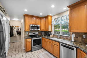 Kitchen featuring appliances with stainless steel finishes, dark stone counters, sink, and tasteful backsplash