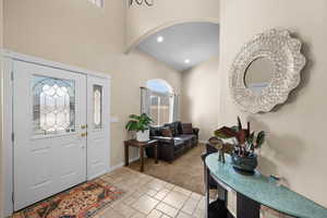 Foyer entrance featuring a towering ceiling, light colored carpet, an inviting chandelier, and plenty of natural light