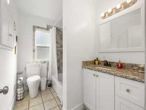 Full bathroom with tile patterned floors, vanity, shower / tub combo with curtain, and toilet