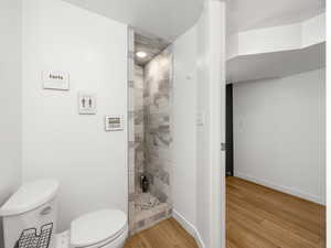 Bathroom with hardwood / wood-style flooring, a tile shower, and toilet