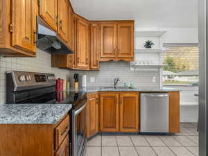 Kitchen with light tile patterned flooring, tasteful backsplash, sink, light stone countertops, and appliances with stainless steel finishes