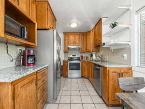 Kitchen featuring light stone counters, light tile patterned floors, sink, tasteful backsplash, and stainless steel appliances