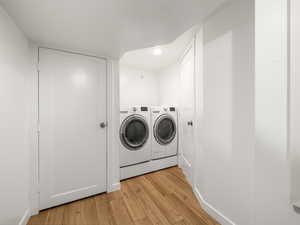 Clothes washing area with light wood-type flooring and washer and dryer