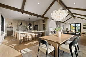 Dining space with vaulted ceiling with beams, an inviting chandelier, and light hardwood / wood-style flooring