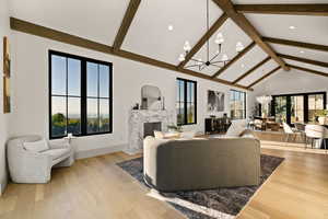 Living room with high vaulted ceiling, light hardwood / wood-style floors, a fireplace, an inviting chandelier, and beam ceiling