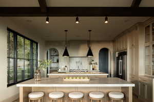 Kitchen with a spacious island, beamed ceiling, stainless steel built in fridge, and a breakfast bar area