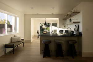 Kitchen with light hardwood / wood-style floors, kitchen peninsula, sink, a breakfast bar, and decorative light fixtures