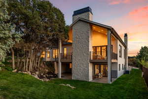 Back house at dusk featuring a lawn, a balcony, and a patio area