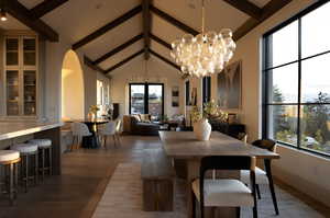 Dining space with hardwood / wood-style flooring, beamed ceiling, an inviting chandelier, and high vaulted ceiling