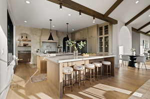 Kitchen with a large island with sink, light hardwood / wood-style floors, beam ceiling, decorative light fixtures, and a kitchen breakfast bar