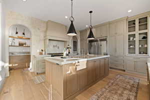 Kitchen featuring a kitchen island with sink, built in refrigerator, hanging light fixtures, light hardwood / wood-style flooring, and cream cabinetry