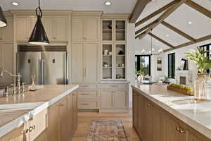 Kitchen featuring light hardwood / wood-style floors, cream cabinets, lofted ceiling with beams, stainless steel built in refrigerator, and hanging light fixtures