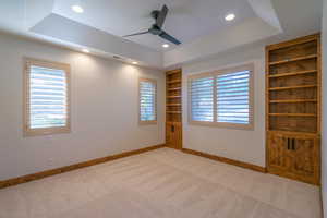 Unfurnished room featuring ceiling fan, a tray ceiling, built in features, and light colored carpet