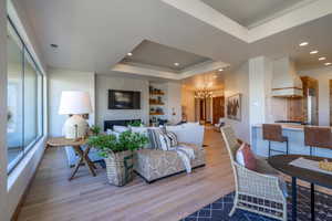 Living room featuring a fireplace, a tray ceiling, an inviting chandelier, and light hardwood / wood-style floors