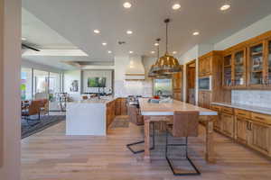 Kitchen with premium range hood, kitchen peninsula, tasteful backsplash, built in appliances, and light hardwood / wood-style floors