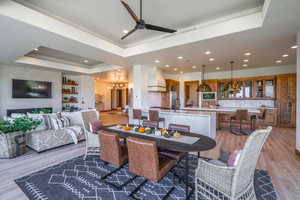 Dining space with ceiling fan with notable chandelier, a tray ceiling, and hardwood / wood-style floors