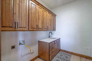 Clothes washing area with sink, hookup for an electric dryer, light hardwood / wood-style flooring, cabinets, and hookup for a washing machine