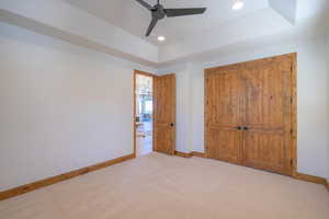 Unfurnished bedroom with ceiling fan, a tray ceiling, a closet, and light colored carpet