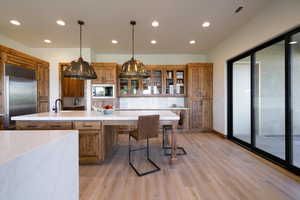 Kitchen with tasteful backsplash, decorative light fixtures, a large island with sink, light hardwood / wood-style flooring, and built in appliances