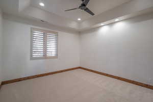 Empty room with light carpet, a tray ceiling, and ceiling fan