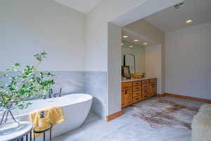 Bathroom with tile patterned flooring, a tub to relax in, vanity, and tile walls