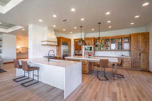 Kitchen with pendant lighting, custom exhaust hood, built in appliances, and a kitchen bar