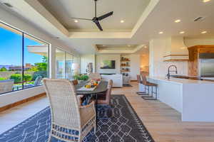 Dining room with light wood-type flooring, ceiling fan, sink, and a raised ceiling