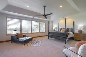 Bedroom with a raised ceiling, light carpet, multiple windows, and ceiling fan