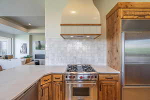 Kitchen with custom range hood, kitchen peninsula, high end appliances, and tasteful backsplash