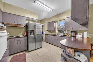 Kitchen featuring stainless steel refrigerator with ice dispenser, sink, white electric cooktop, light tile patterned floors, and gray cabinetry