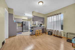 Kitchen with a kitchen breakfast bar, kitchen peninsula, stainless steel refrigerator with ice dispenser, light hardwood / wood-style flooring, and gray cabinets