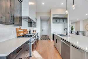 Kitchen featuring appliances with stainless steel finishes, sink, light stone counters, and pendant lighting