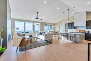 Living room featuring light wood-type flooring, vaulted ceiling, ceiling fan with notable chandelier, and sink