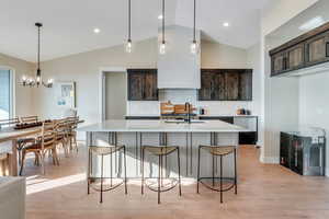 Kitchen with decorative backsplash, decorative light fixtures, a kitchen island with sink, dark brown cabinets, and sink